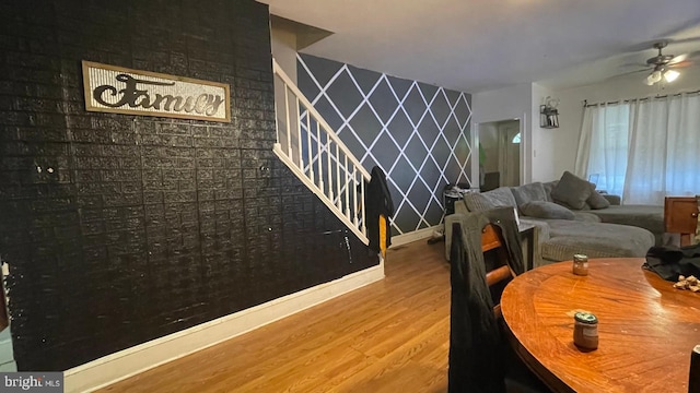 dining area featuring an accent wall, wood finished floors, baseboards, and a ceiling fan