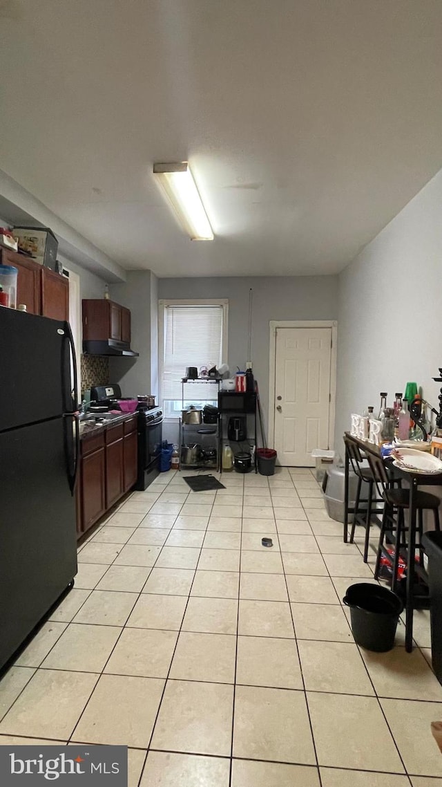 kitchen featuring light tile patterned floors, dark countertops, black appliances, and under cabinet range hood