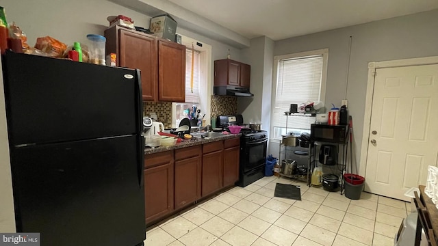 kitchen featuring dark countertops, under cabinet range hood, light tile patterned floors, decorative backsplash, and black appliances