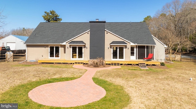 back of house featuring a lawn, roof with shingles, a chimney, and fence