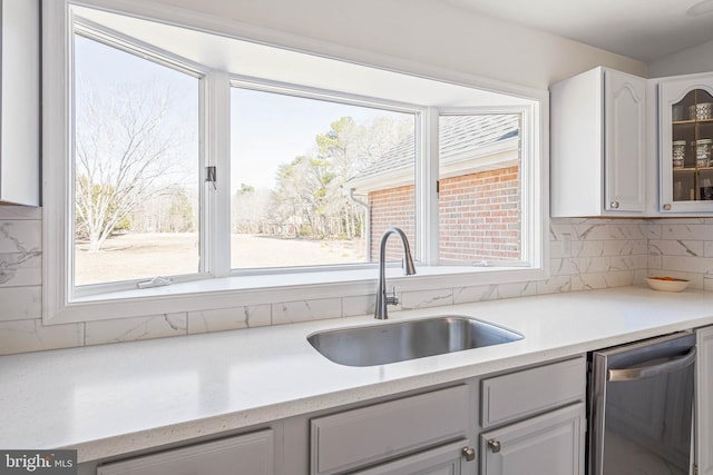 kitchen with a sink, stainless steel dishwasher, backsplash, white cabinets, and glass insert cabinets