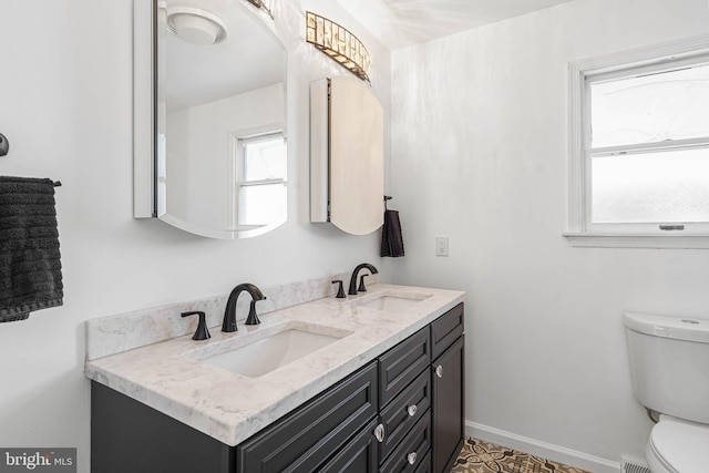 bathroom with double vanity, toilet, baseboards, and a sink