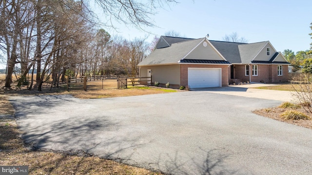 view of front of home with brick siding, fence, aphalt driveway, a garage, and a standing seam roof