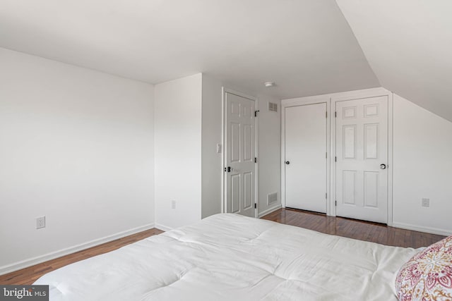 bedroom with vaulted ceiling, visible vents, baseboards, and wood finished floors