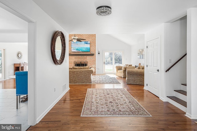 entrance foyer featuring visible vents, stairway, wood-type flooring, a brick fireplace, and vaulted ceiling