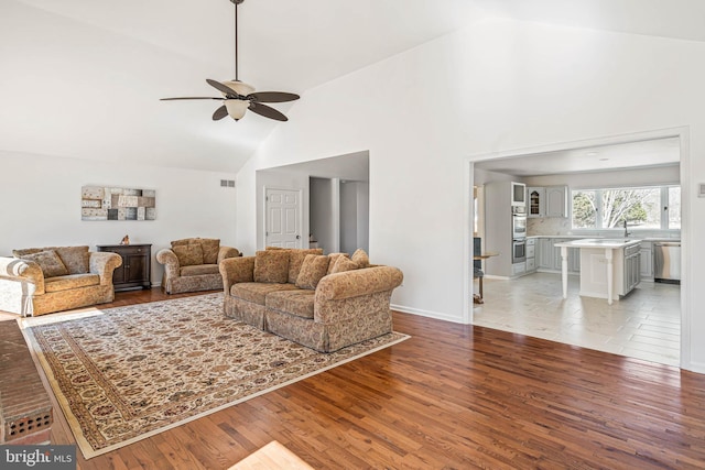 living room featuring visible vents, high vaulted ceiling, a ceiling fan, light wood finished floors, and baseboards