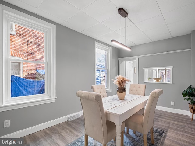 dining area with visible vents, a drop ceiling, baseboards, and wood finished floors