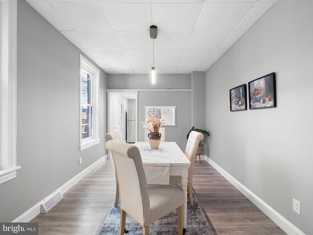 dining space with visible vents, wood finished floors, baseboards, and a drop ceiling