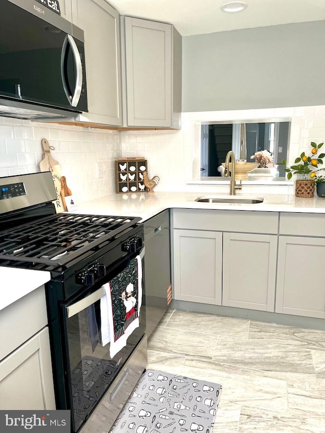 kitchen featuring light countertops, tasteful backsplash, stainless steel gas stove, and a sink