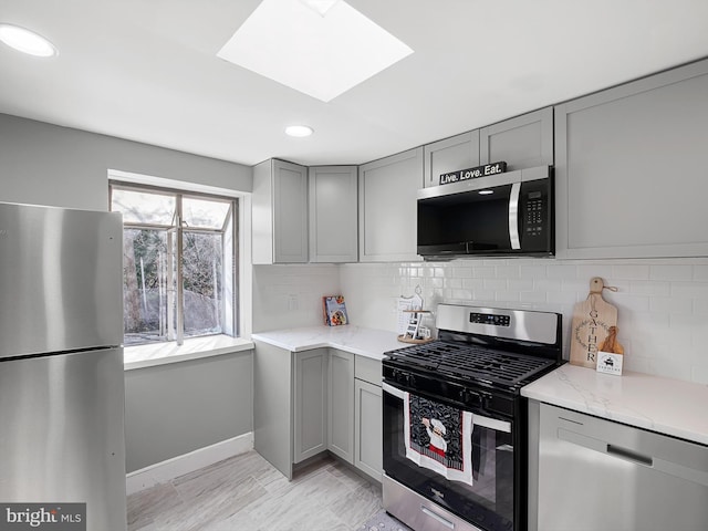 kitchen featuring light stone counters, gray cabinets, backsplash, and stainless steel appliances