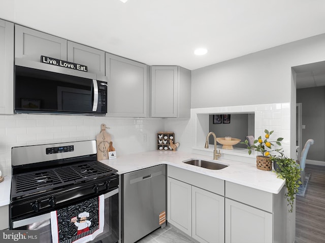 kitchen with light stone counters, gray cabinets, stainless steel appliances, and a sink