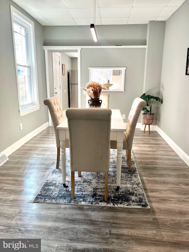 unfurnished dining area with baseboards, a paneled ceiling, and wood finished floors