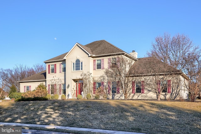 view of front of house featuring stucco siding, a chimney, a front yard, and a shingled roof