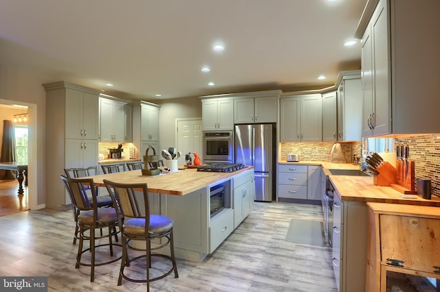 kitchen with light wood finished floors, butcher block counters, appliances with stainless steel finishes, a kitchen breakfast bar, and a center island