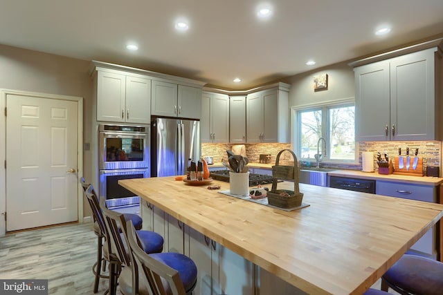 kitchen featuring decorative backsplash, recessed lighting, a kitchen breakfast bar, stainless steel appliances, and wood counters