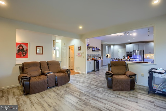 living room with recessed lighting, baseboards, a bar, and light wood-style flooring