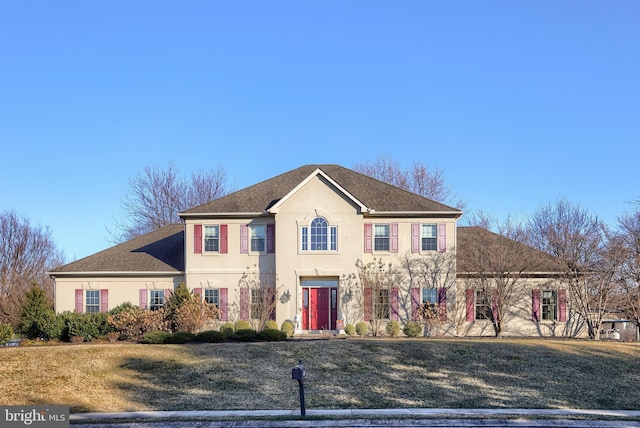 view of front facade with stucco siding, a front yard, and roof with shingles