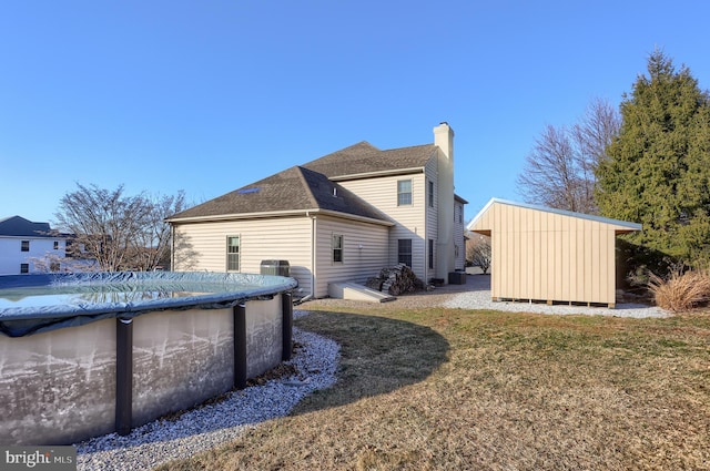 view of side of property with an outbuilding, a lawn, a covered pool, a shingled roof, and a chimney