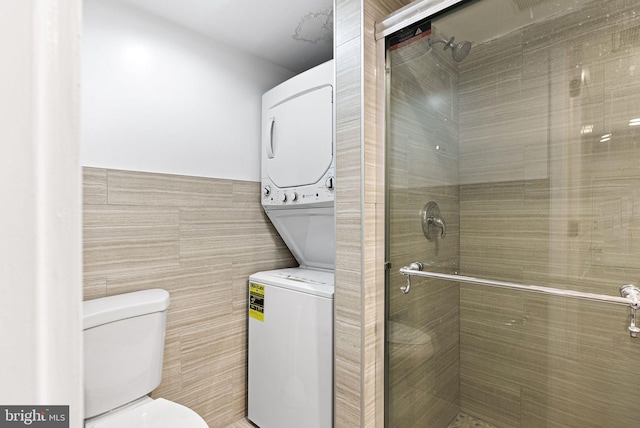 bathroom featuring a shower stall, toilet, tile walls, and stacked washer and clothes dryer