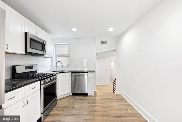 kitchen with dark countertops, visible vents, light wood-style flooring, appliances with stainless steel finishes, and a sink