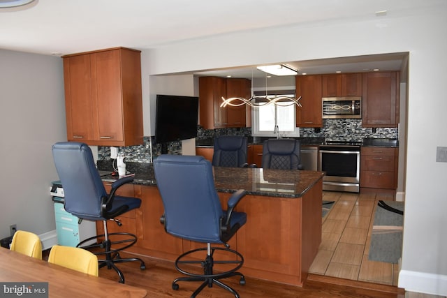 kitchen with brown cabinets, a peninsula, appliances with stainless steel finishes, and tasteful backsplash