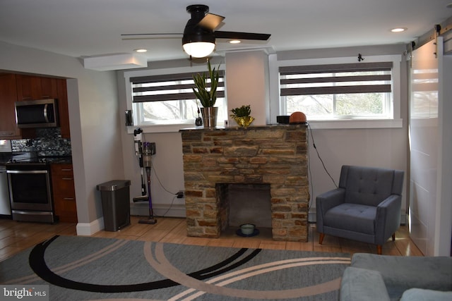 living area with a wealth of natural light, ceiling fan, light wood-style floors, and a barn door