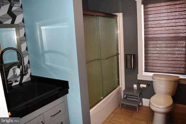 full bath with wood finished floors, enclosed tub / shower combo, toilet, vanity, and baseboards