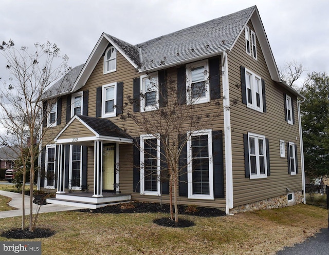 colonial inspired home featuring a front lawn, fence, and a shingled roof