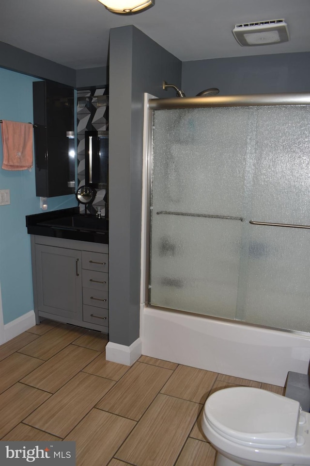 bathroom with shower / bath combination with glass door, toilet, vanity, visible vents, and wood tiled floor