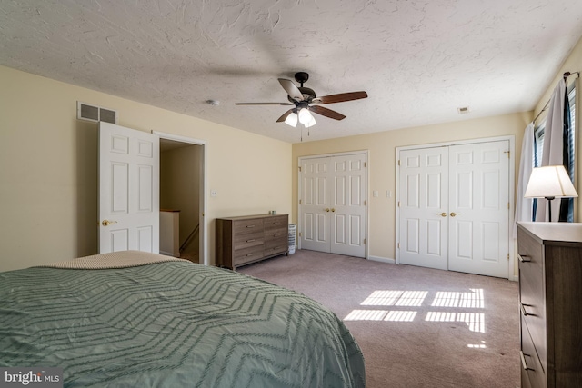 bedroom featuring visible vents, ceiling fan, multiple closets, a textured ceiling, and light carpet