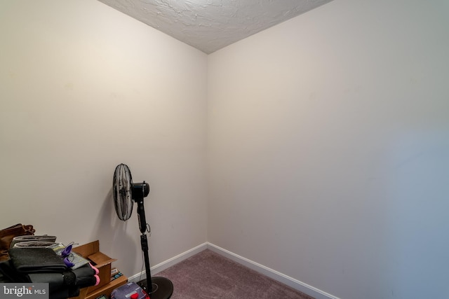 interior space featuring baseboards, a textured ceiling, and dark carpet