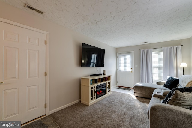 carpeted living room with visible vents, a textured ceiling, baseboards, and a glass covered fireplace