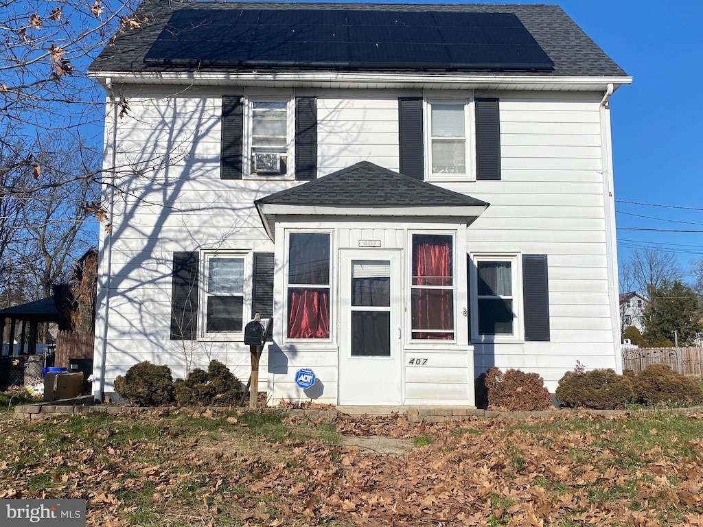 view of front of house featuring solar panels, fence, and roof with shingles