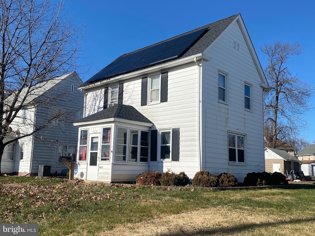 view of side of home featuring cooling unit, roof with shingles, a sunroom, a lawn, and roof mounted solar panels