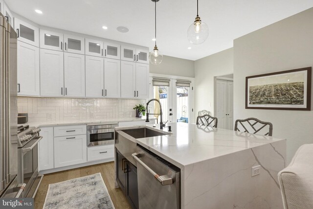 kitchen with a sink, stainless steel appliances, light stone counters, and white cabinetry