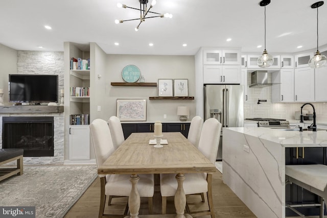 dining space featuring light wood finished floors, a stone fireplace, recessed lighting, and built in features