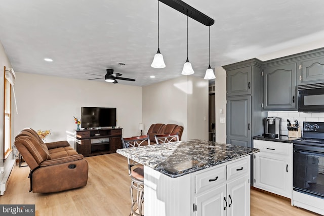 kitchen with dark stone counters, light wood-style flooring, black appliances, backsplash, and a center island