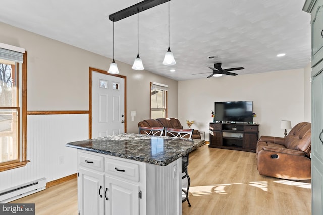 kitchen with a kitchen island, a baseboard heating unit, open floor plan, light wood-style floors, and white cabinetry