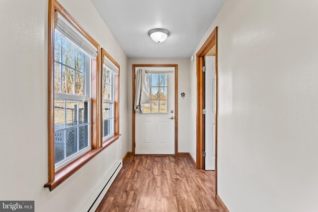 doorway to outside featuring a baseboard heating unit, baseboards, and light wood-type flooring