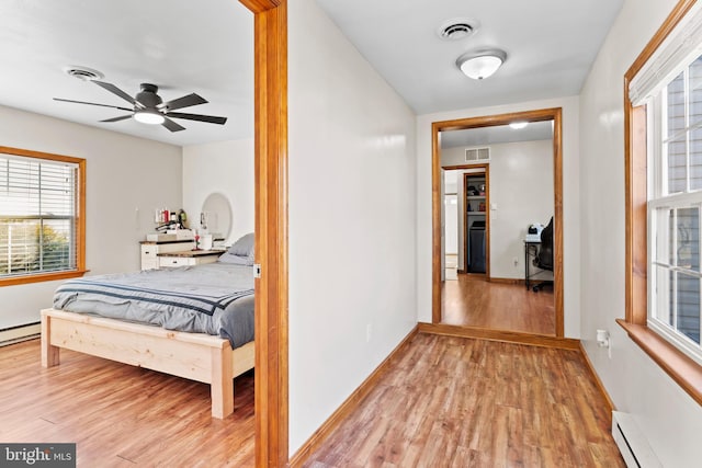 hall featuring light wood-type flooring, a baseboard heating unit, and visible vents