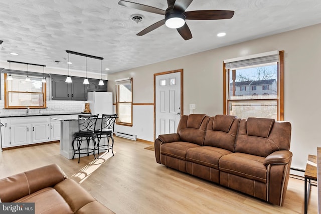 living room featuring a baseboard heating unit, baseboard heating, light wood-style floors, a textured ceiling, and a ceiling fan