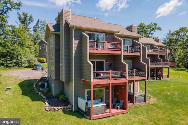 back of house featuring a hot tub, a shingled roof, central air condition unit, a chimney, and a yard