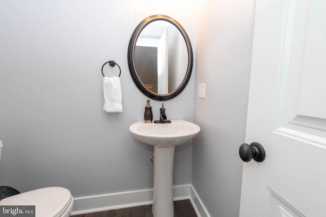 half bath with a sink, baseboards, toilet, and wood finished floors