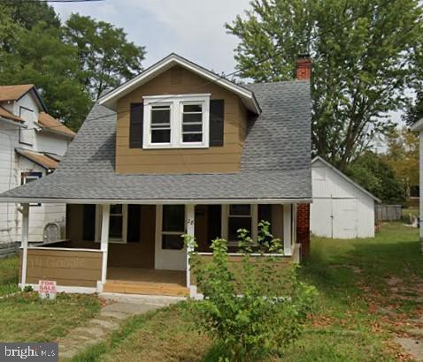 view of front of home with a chimney, covered porch, a front lawn, and a shingled roof