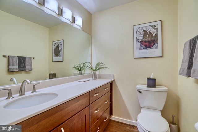 bathroom with vanity, toilet, wood finished floors, and baseboards