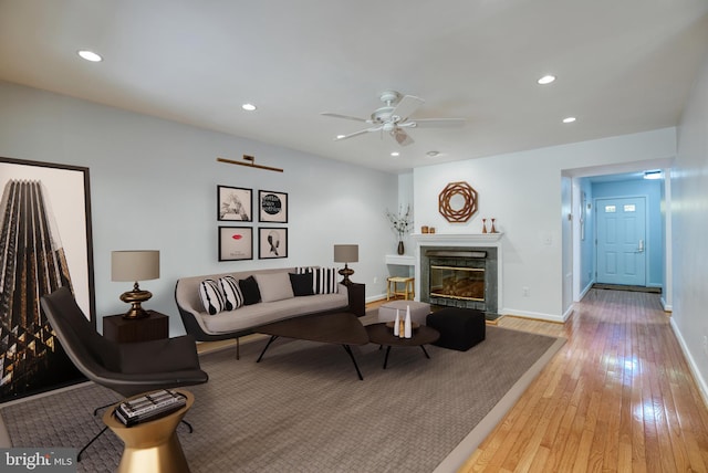 living area with a ceiling fan, baseboards, light wood-style flooring, a fireplace with flush hearth, and recessed lighting