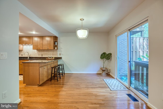 kitchen featuring light wood-style flooring, open shelves, tasteful backsplash, dark countertops, and a breakfast bar area