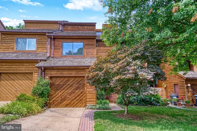 view of property with a garage, roof with shingles, concrete driveway, and a front yard