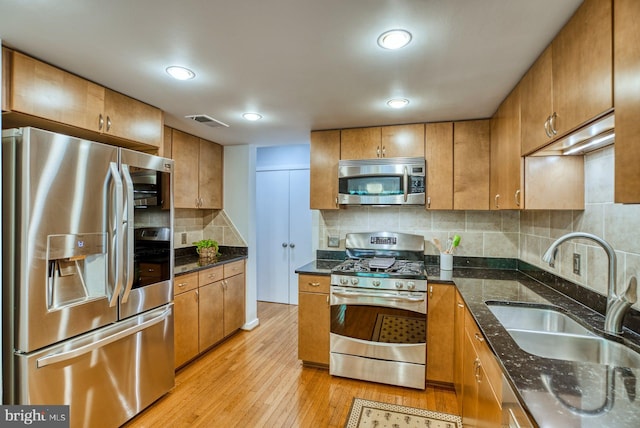 kitchen featuring visible vents, brown cabinets, appliances with stainless steel finishes, light wood-style floors, and a sink