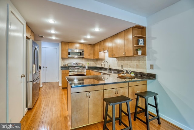 kitchen featuring a sink, open shelves, stainless steel appliances, a peninsula, and light wood finished floors